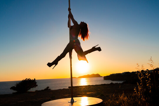 White woman performing pole dance in silhouette
