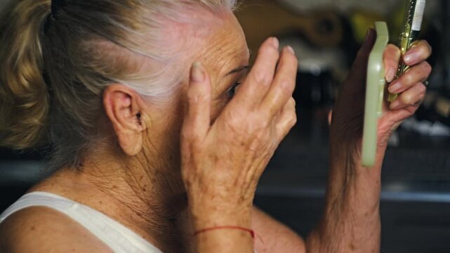 Senior woman applying mascara to her eyebrows and eyelashes herself in a home kitchen studio demonstrating independence and personal care in old age