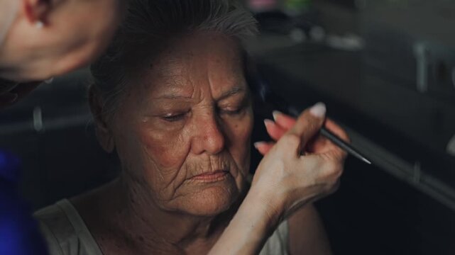 Young woman gently brushing cream onto the face of an elderly woman during a home beauty care routine