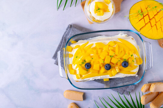 Tiramisu cake with mango topped with fruit pieces served in the glass dish. Italian layered dessert variation. Top view. Space for text