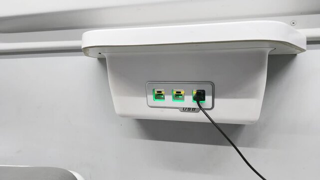 Charging phone using USB outlet inside train compartment. charge process shown in closeup, charging cable connected to socket, modern travel comfort, public transport interior, mobility concept