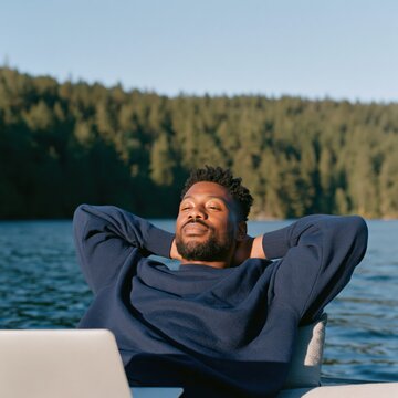 Relaxed man reclining by a lake with a laptop for remote work lifestyle background and wellness banner design