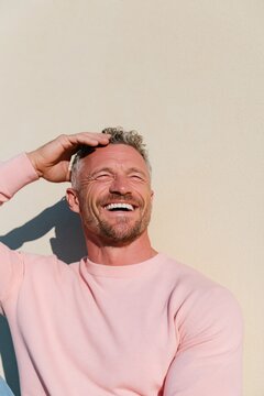 Smiling man in pink sweater against beige wall for lifestyle portrait background and social media profile use