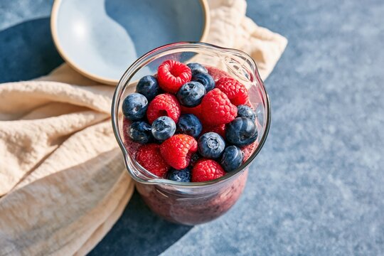 Overhead beaker of mixed raspberries and blueberries smoothie in glass jug for nutritious breakfast background and seasonal healthy drink design