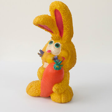 A vintage yellow textured bunny rabbit toy holding a bright orange carrot, isolated on a clean white background. Perfect for Easter or retro toy concepts.