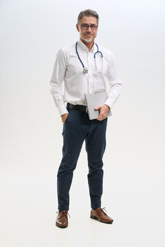 Full length portrait of doctor, general practitioner, physician, medical professional with tablet on white, Mid adult, mature age man happy smiling.