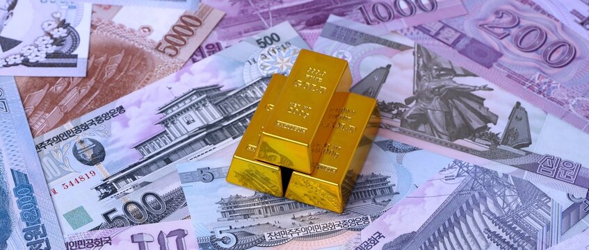 North Korean won money bills and gold bullion bars. North Korea cash bills of KPW currency close up