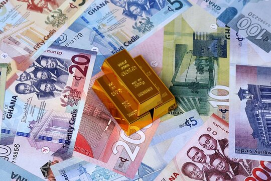 Ghanaian cedi money bills and gold bullion bars. Ghana cash bills of GHS currency close up