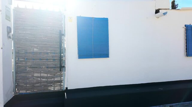 White house wall with blue shutter and bamboo gate