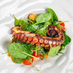 Grilled octopus tentacle with spinach leaves, cherry tomatoes, sauce, and golden garnish arranged on a white plate in an overhead seafood dish © Надія Коваль