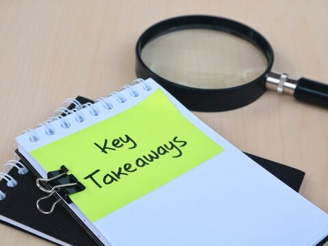 Key takeaways handwritten text on green adhesive note attached to spiral book with magnifying glass on wooden background, high angle view. Business summary, review, and key points concept