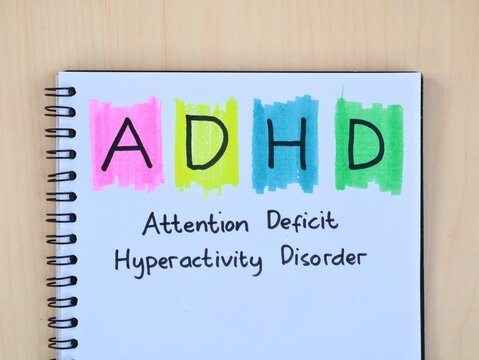 Handwritten ADHD (Attention Deficit Hyperactivity Disorder) on spiral book on wooden desk, top view.  Perfect for education, childhood, and mental health awareness concept