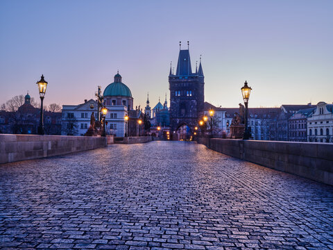 Empty Charles Bridge with glowing lamps in Prague before sunrise