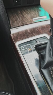 Close up view of a hand shifting the automatic gear lever inside a modern car. The driver moves from drive to neutral, reverse and park