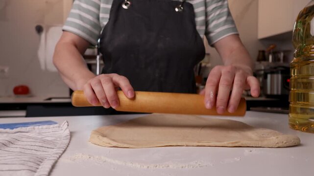 Rolled dough being flattened into a thin sheet in a warm home kitchen with a rolling pin