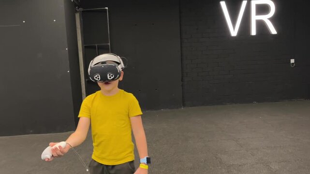 A boy in yellow T-shirt immerses himself in virtual reality. Playing virtual reality game with headset. A party children's center. Modern technology, VR games, and digital entertainment for children.