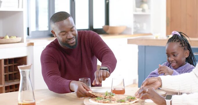 African American family in kitchen fresh pizza leading father slicing with cutter handing teen girl