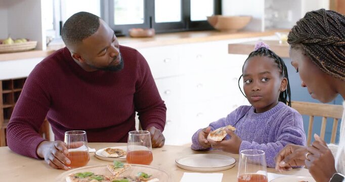 African family sharing pizza at table daughter in purple checking slice offering father taking bite