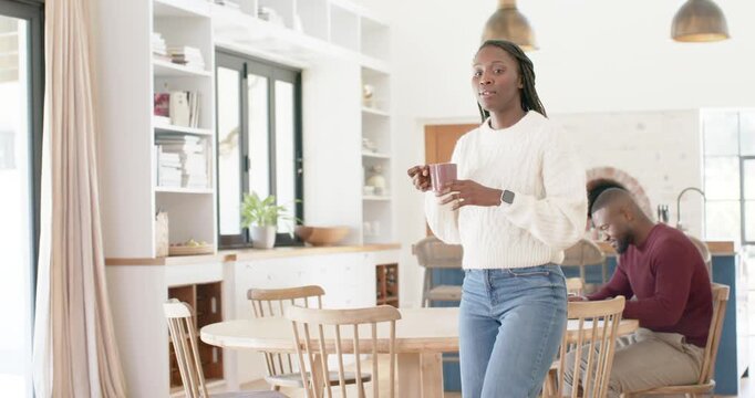 African American family mom carrying mug walking to couch, adjusting cushion and checking daughter