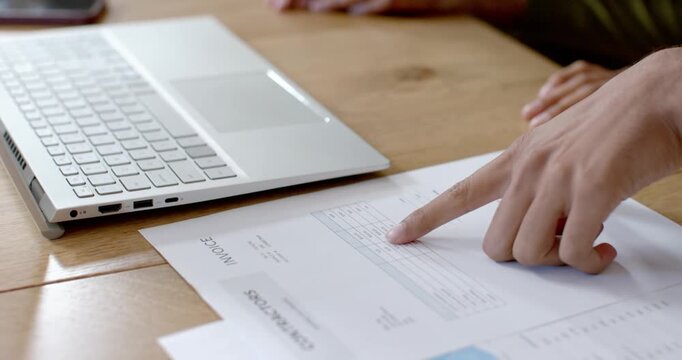 Hand entering frame is sliding invoice near laptop, pointing at HOUSE BUDGET chart to review costs