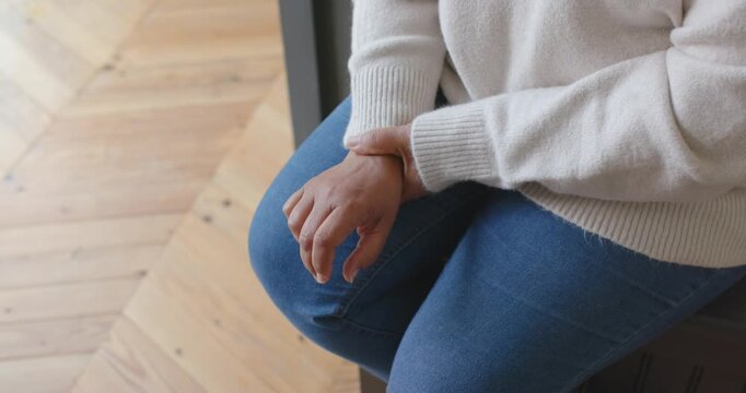 After sitting, woman is shifting left hand and massaging right wrist on lap to ease tension
