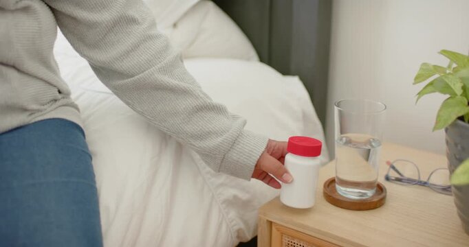 African American mature woman reaching and checking bottle with red cap at bedside for morning dose