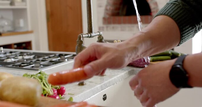 Cook's hands are rinsing carrots at kitchen sink with brass faucet being turned on for cooking