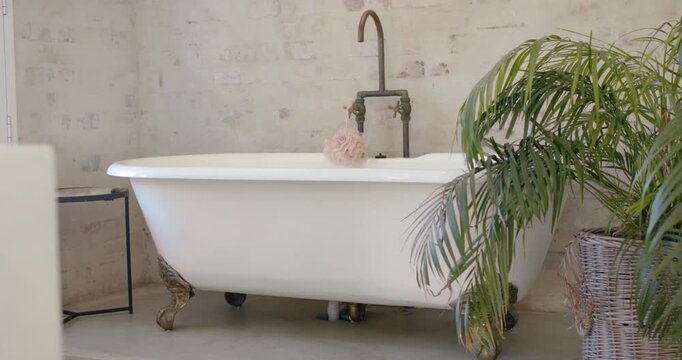 Camera is panning left, revealing tub with pouf and brass faucet showing bathroom vignette