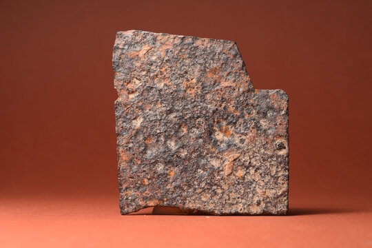 A flat, rectangular fragment of heavily corroded and rusted iron. Isolated studio shot on a brown background.