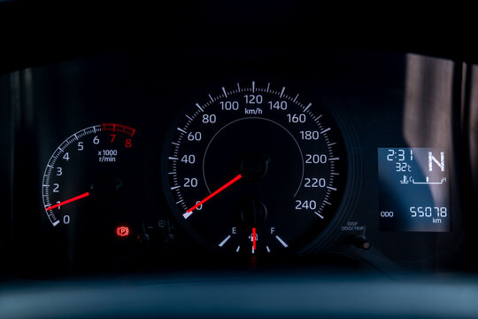 Close up of modern car dashboard speedometer and tachometer gauge panel displaying fuel level, engine temperature, mileage odometer, gear indicator and parking brake warning light.