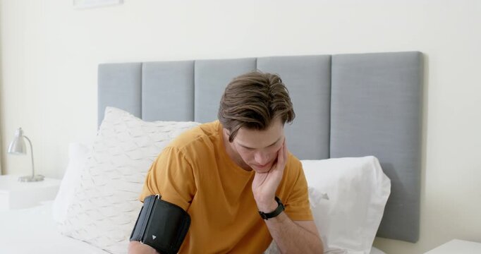Adult man sitting on bed after securing black cuff watching white unit and checking blood pressure