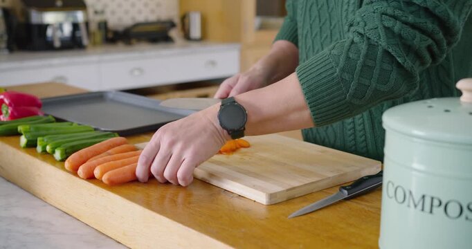 Hands are placing cutting board on counter with carrots, picking up knife and slicing for roasting