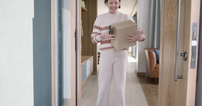 Woman checking phone confirming drop opening door at home picking parcel from mat bringing to table