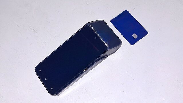 Modern EDC POS terminal machine with blue credit card on white table surface top view copy space