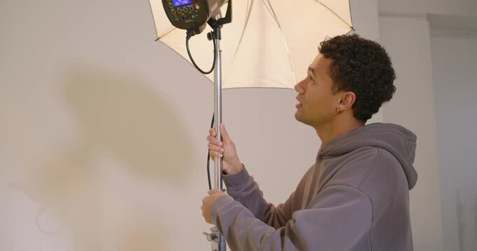 Diverse crew in studio preparing portrait, tech adjusting strobe as shooter firing DSLR at model