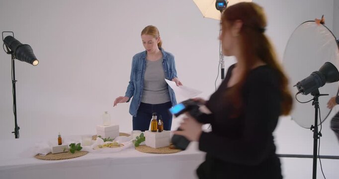 Stylist photographer and assistant arranging amber bottles while using shot list in white studio