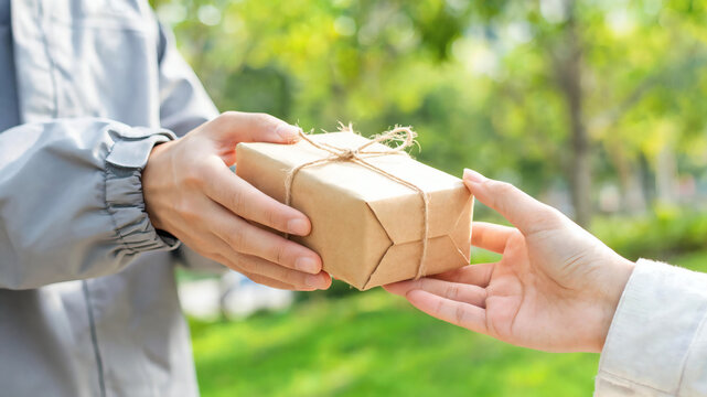 Close up shot of courier hands handing over a small sustainable brown paper parcel tied with natural string to a customer