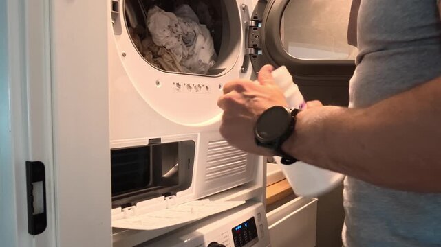 Man performing routine maintenance of a household tumble dryer, removing lint and dust from the filter compartment using a vacuum cleaner, cleaning brush and cloth. Domestic appliance cleaning and hom