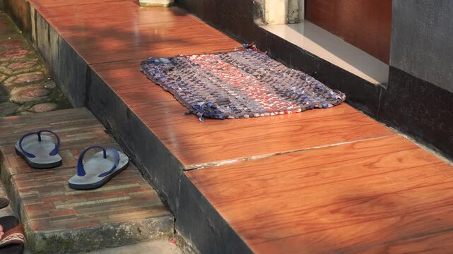 Barefoot person leaving flip-flops and wiping feet on a doormat before entering.