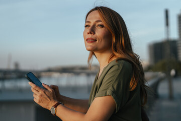 Naklejka premium Woman holding smartphone reflecting at sunset cityscape