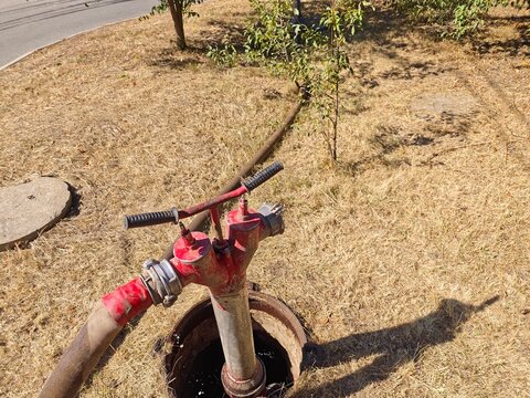 High angle view of a red fire hydrant standpipe with a connected long hose leading to a road during municipal water extraction on dry grass.