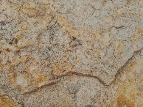 the natural texture of a stone surface with unique patterns and a variety of colors, ranging from beige and gray to brown and golden ochre. The surface features natural streaks, fine grains, small cra