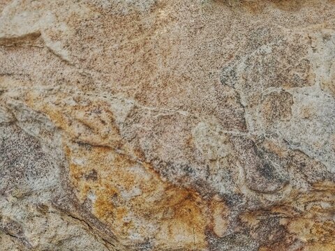the natural texture of a stone surface with unique patterns and a variety of colors, ranging from beige and gray to brown and golden ochre. The surface features natural streaks, fine grains, small cra