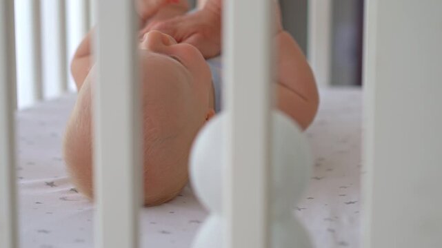 Close-up of mother stroking five-month-old son in crib with baby monitor camera in foreground. Infant care