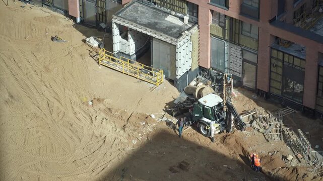 Heavy machinery excavating a deep pit on a construction site, while a worker in overalls stands by and supervises the earthmoving operation during a sunny day. Powerful excavator bucket extracts groun