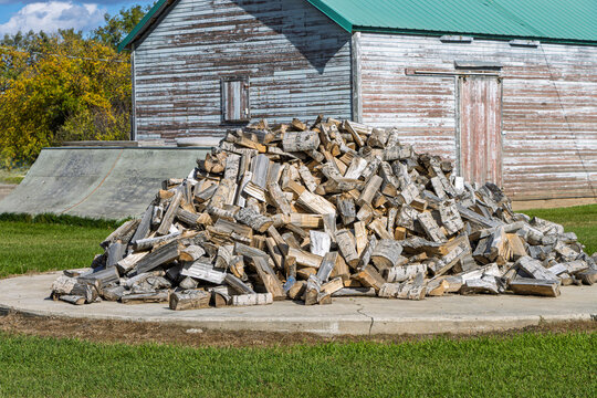 Large Pile of Split Firewood Beside a Weathered Wooden Barn