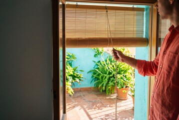 Fototapeta premium Man opening bamboo blinds on sunny terrace