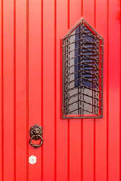 Red Paneled Door With Lion Knocker And Narrow Grilled Window On Urban Facade