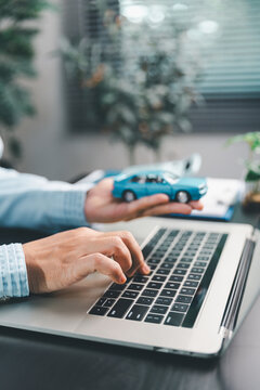 Hands using a laptop while holding a toy car, illustrating online auto insurance quotes, digital vehicle finance, policy comparison, purchase research, financial planning and remote customer service.