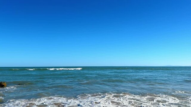 Blue ocean seascape with small waves and clear sky. Wide angle view of sea surface with mild ripples reaching the horizon under a cloudless atmosphere.